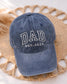 Single Ball Cap with adjustable strap featuring an embroidered DAD est date logo - placed on a woven placemat for photo