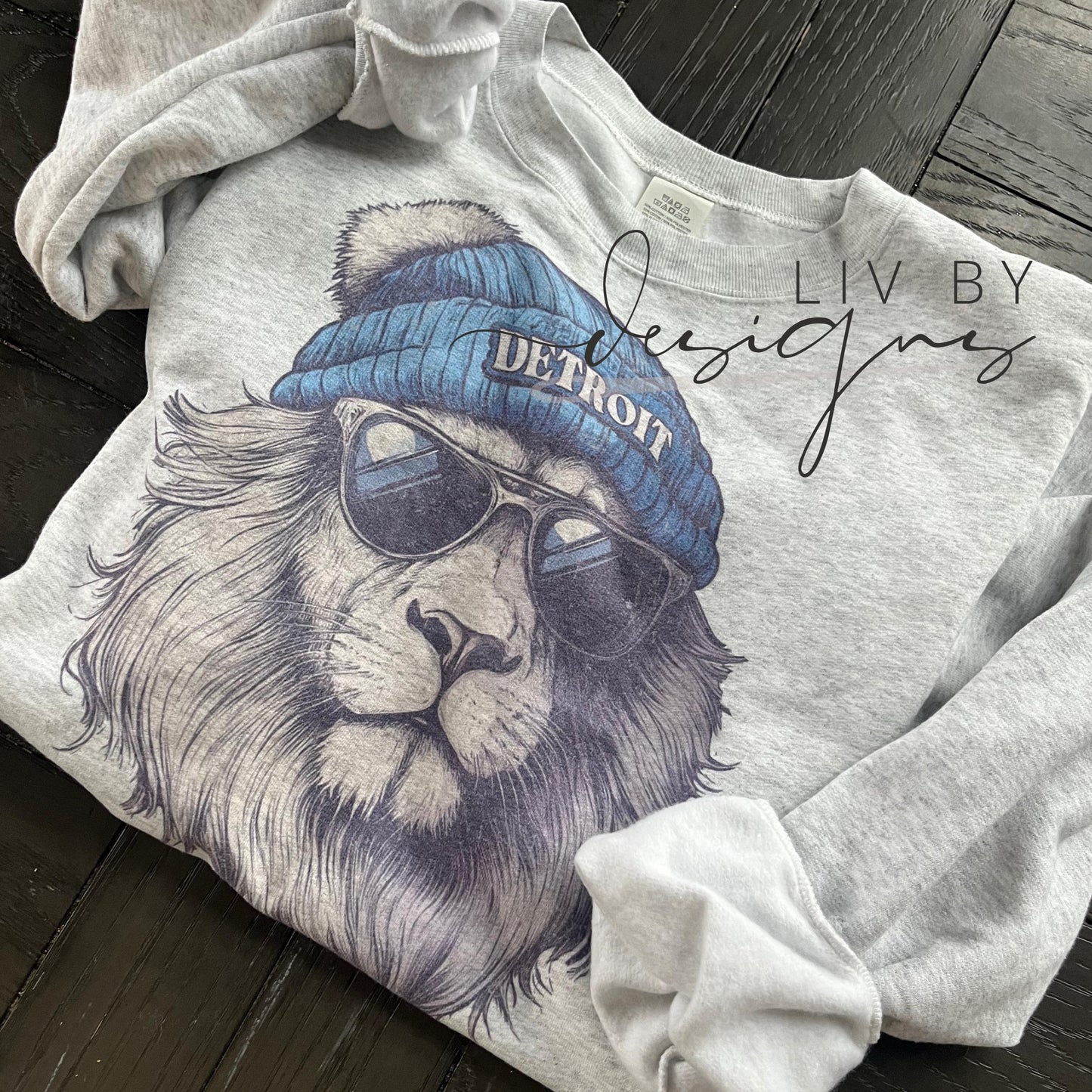 A gray sweatshirt with a graphic of a lion wearing a blue beanie with the word "DETROIT" on it and sunglasses.