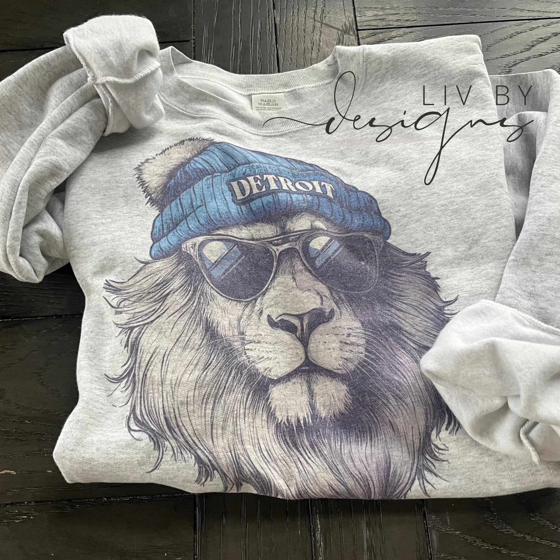 A gray sweatshirt with a graphic of a lion wearing a blue beanie with the word "DETROIT" on it and sunglasses.