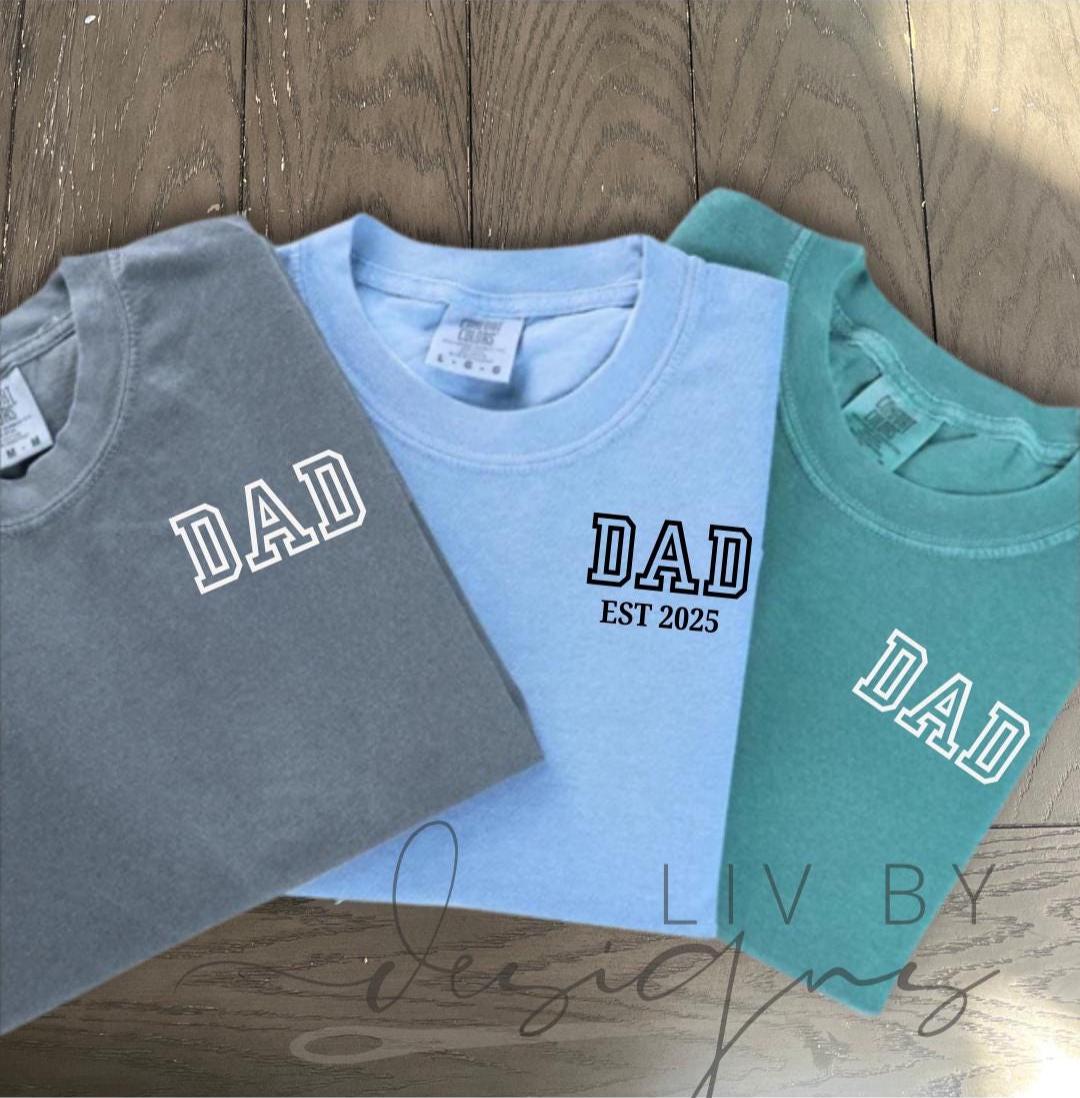 “Three Comfort Colors DAD EST shirts in gray, blue jean, and chalky mint stacked on wood background” (etsy image id: 6936738119)