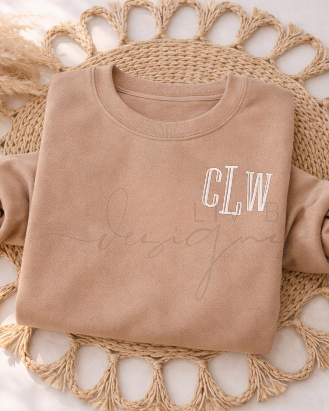 Embroidered monogram Bella and Canvas crewneck sweatshirt in neutral tan color with white stitched initials, folded flat on woven background. (etsy image id: 7613596714)