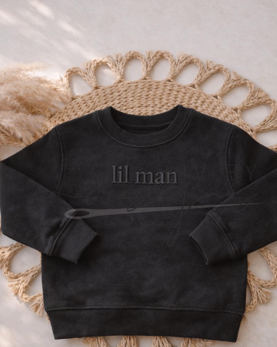 A simple laid out image of a rabbit skins black crewneck featuring an embroidered "lil man" on the front of his chest with a monochrome coloring thread (etsy image id: 7660006889)